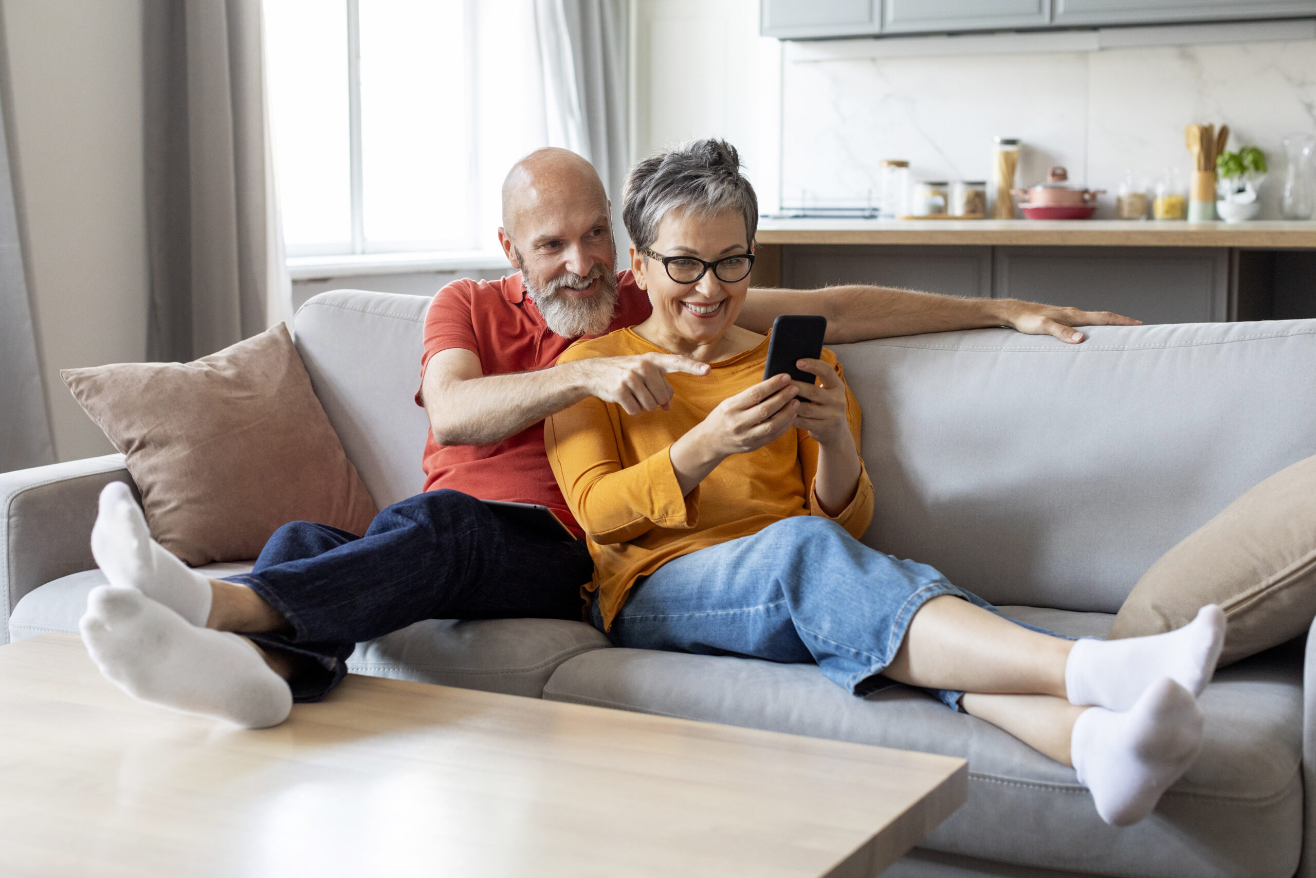 happy senior couple using smartphone and embracing together at home