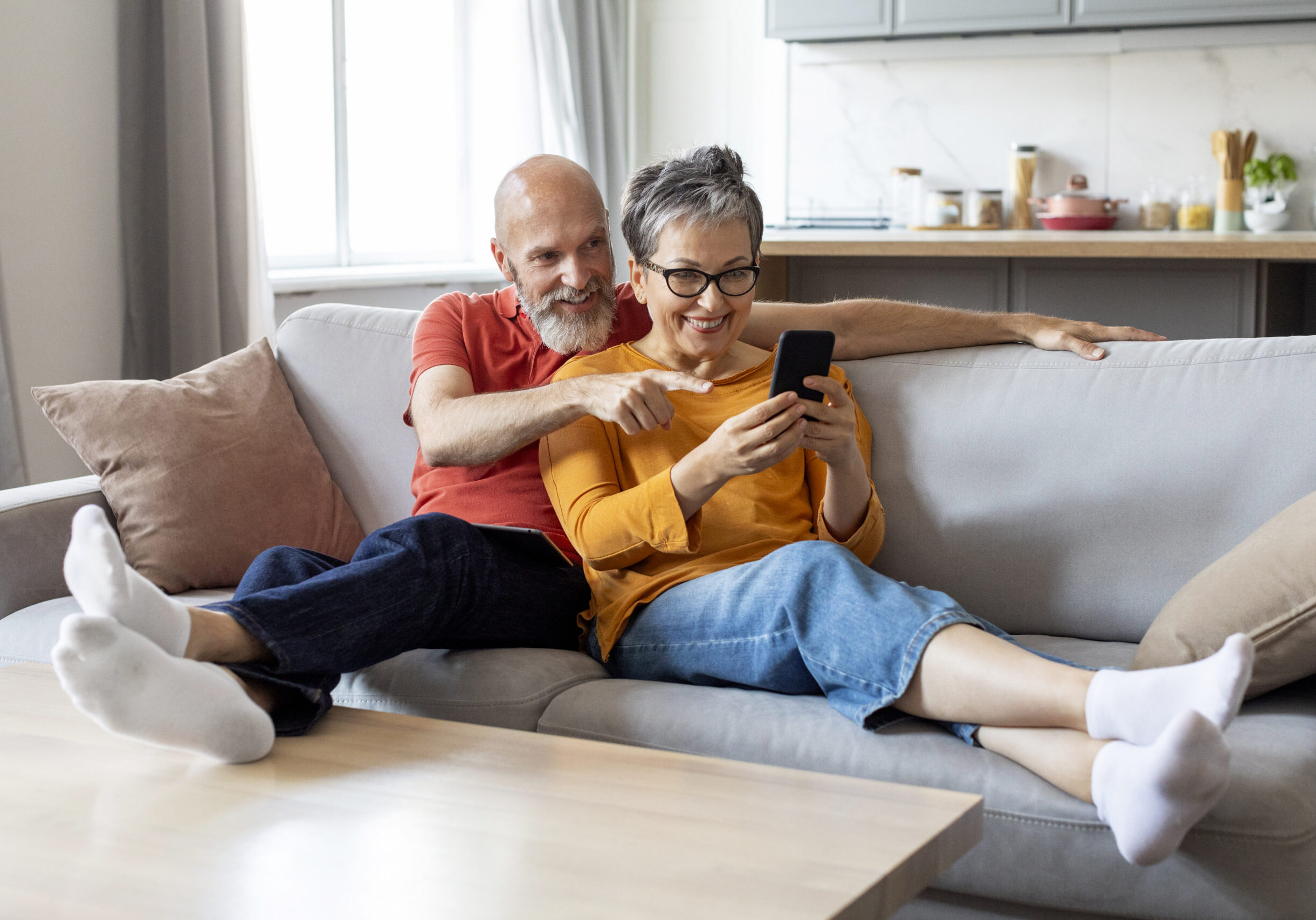 happy senior couple using smartphone and embracing together at home